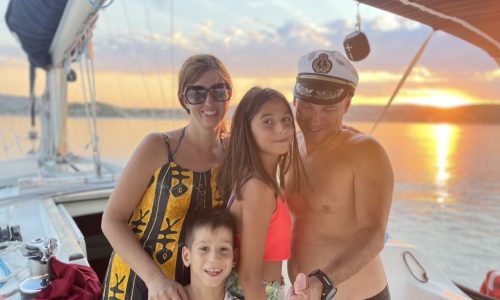 A family in the cockpit of our spacious Jeanneau Sun Odyssey sailing yacht with a magical sunset in the background.