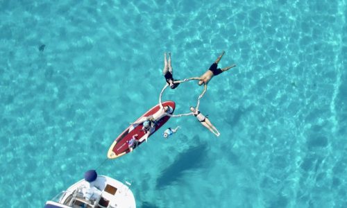 A family with children relaxing on a sup paddle board at the Blue Lagoon during a full day sailing charter to Diaporos island.